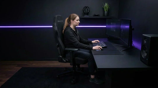 Gamer at an all-black stealth battlestation in an ergonomic matte black gaming chair — long session lumbar support setup